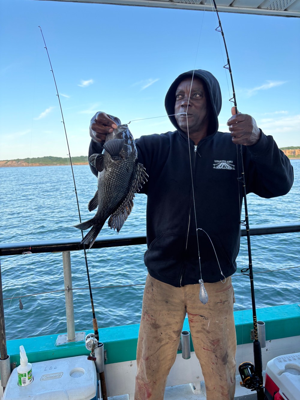 Person holding a fish on a boat with fishing rods and water in the background.