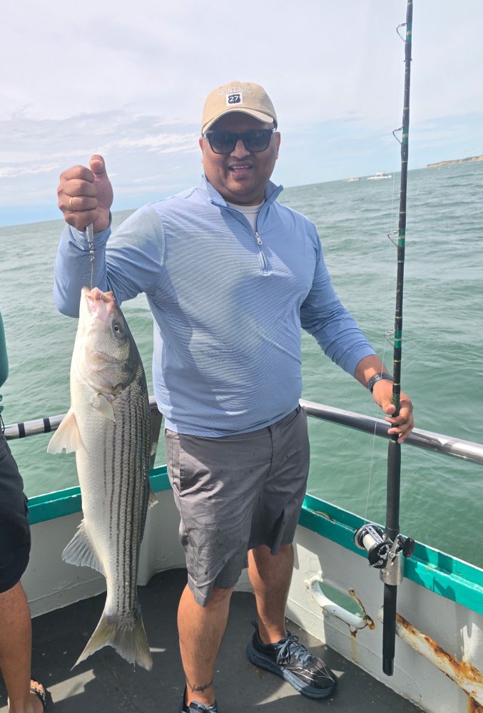 Person holding a large fish on a boat, wearing sunglasses and a cap.
