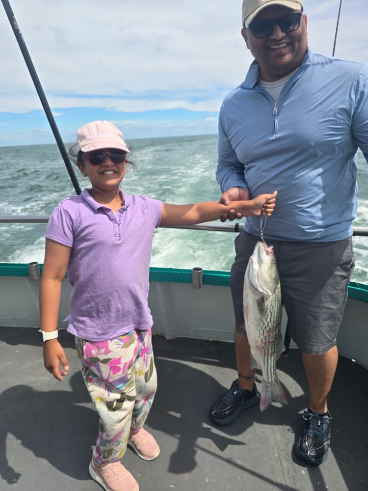 Person and child holding a striped fish on a boat at sea.