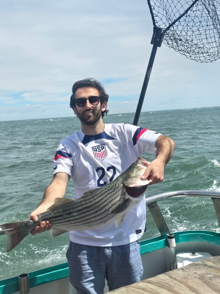 Man on a boat holds a large striped fish on a sunny day.