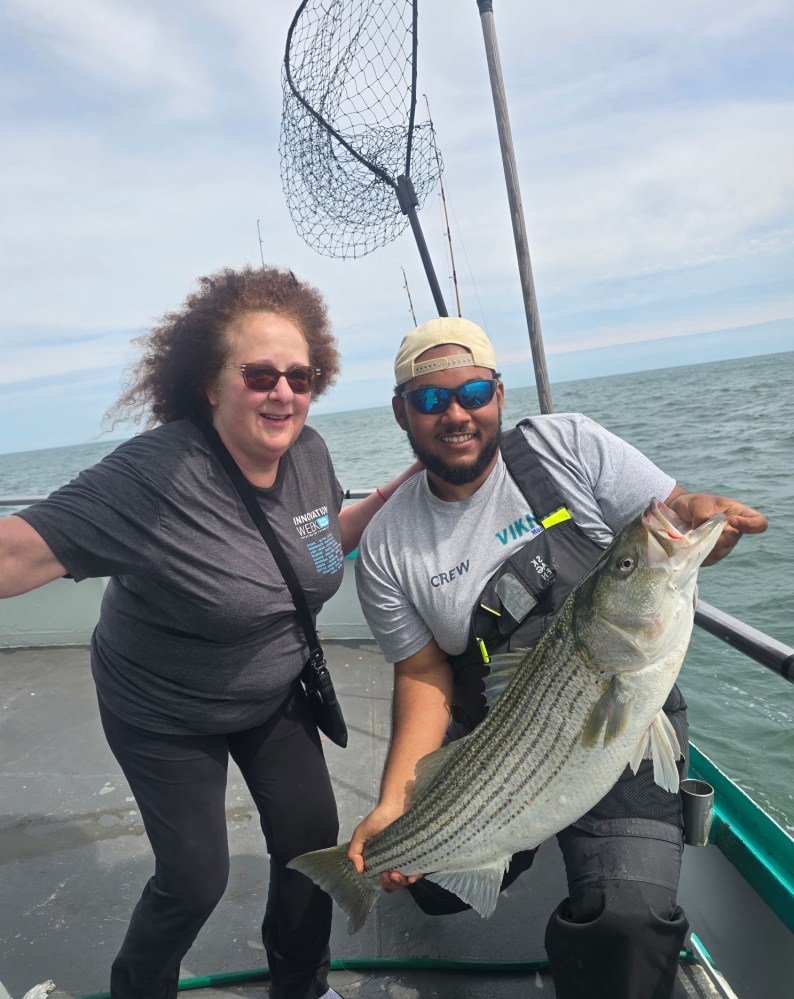 Two people on a boat holding a large fish with a net in the background.