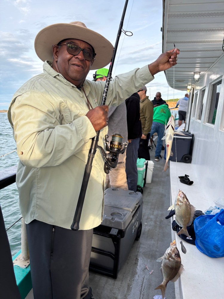 Man on boat holding fishing rod with caught fish, smiling.