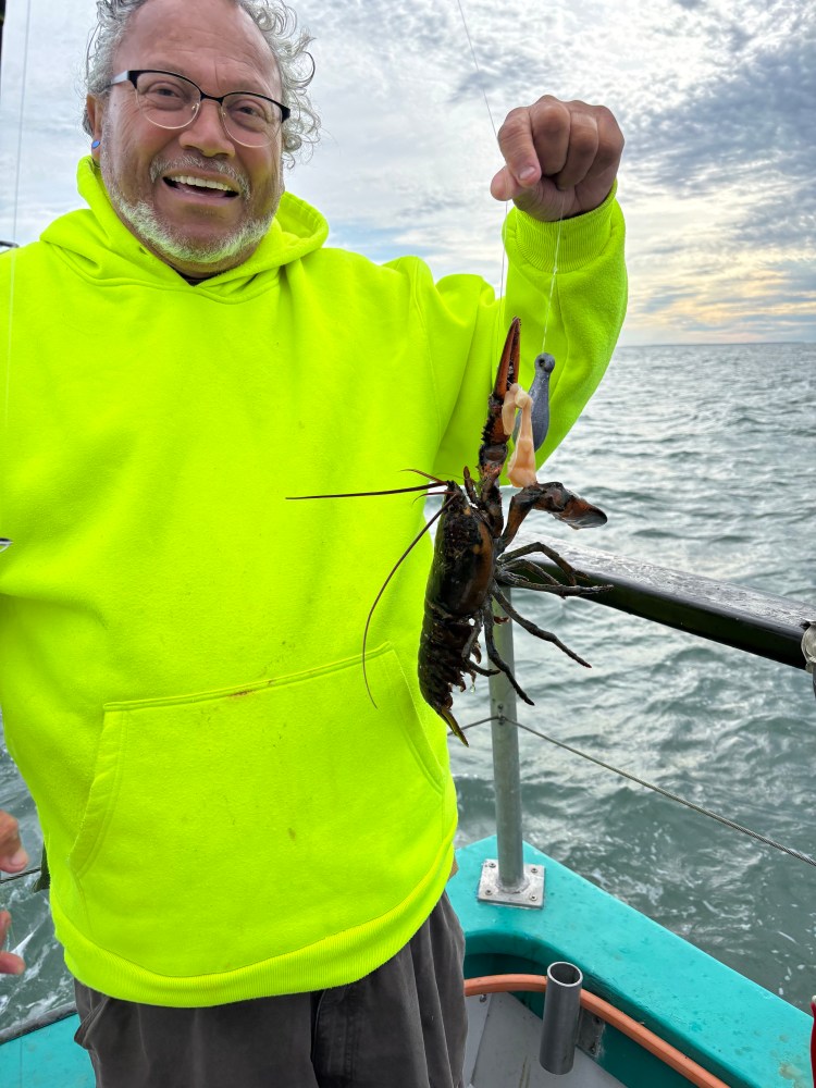 Man in bright hoodie holding lobster on a boat with cloudy sky.