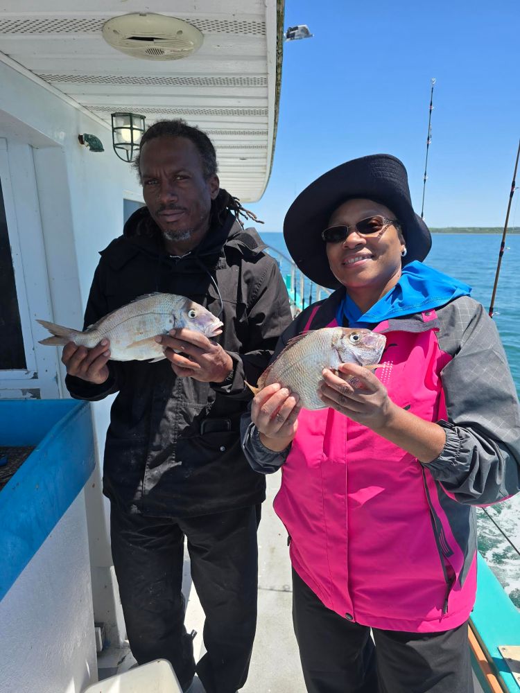 Two people holding fish on a boat with fishing rods visible.