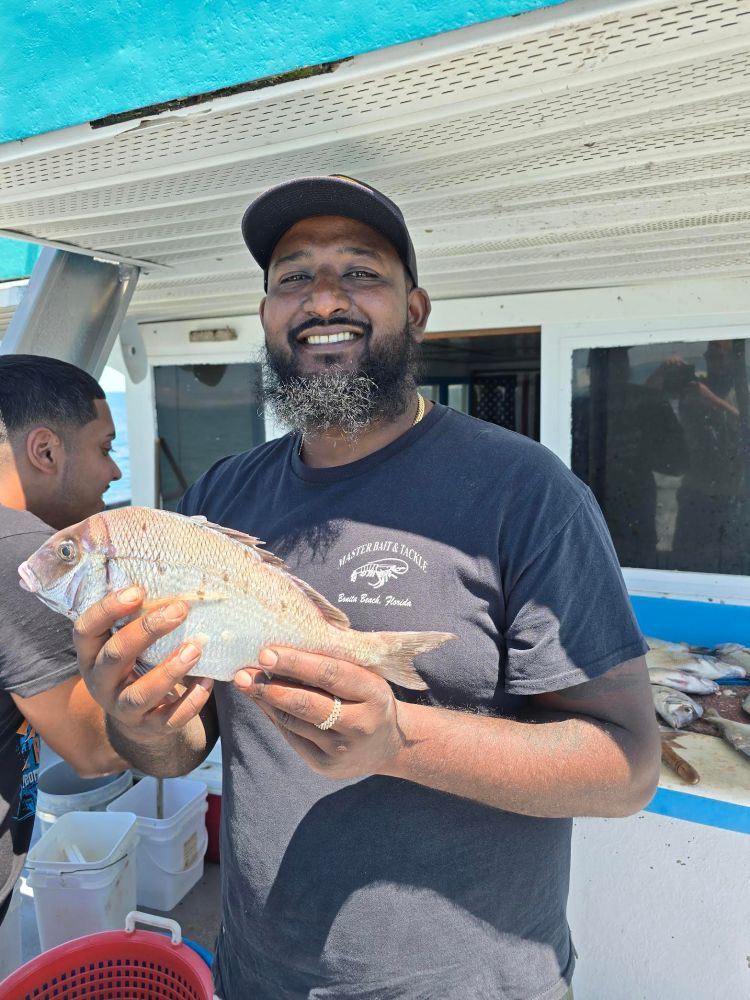 Smiling man holding a fish on a boat, with another person nearby.