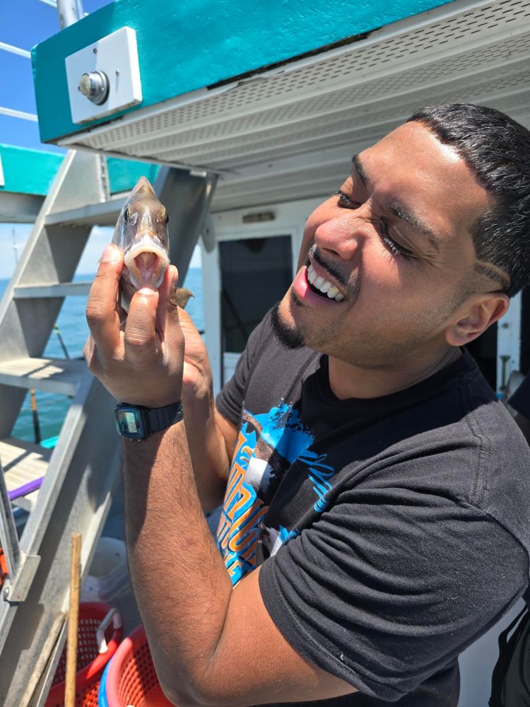 Man smiling while holding a fish on a boat deck.