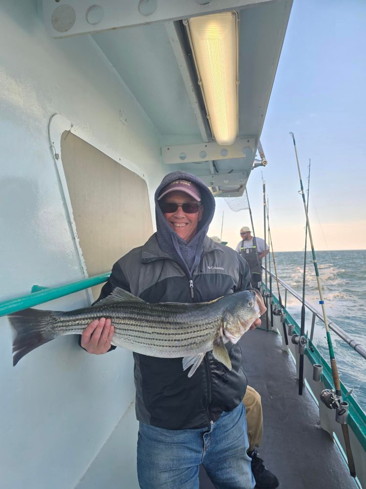 Person smiling, holding a large fish on a boat with ocean in the background.