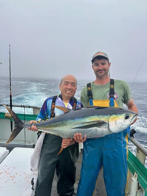 Two men on a boat holding a large fish together.