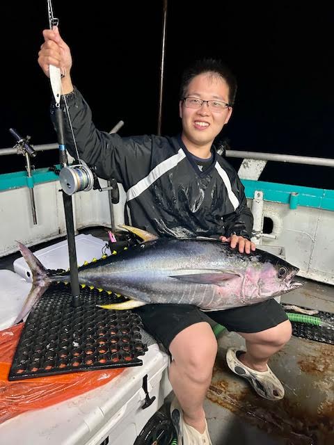Person on a boat holding a fishing rod with a large tuna on their lap.