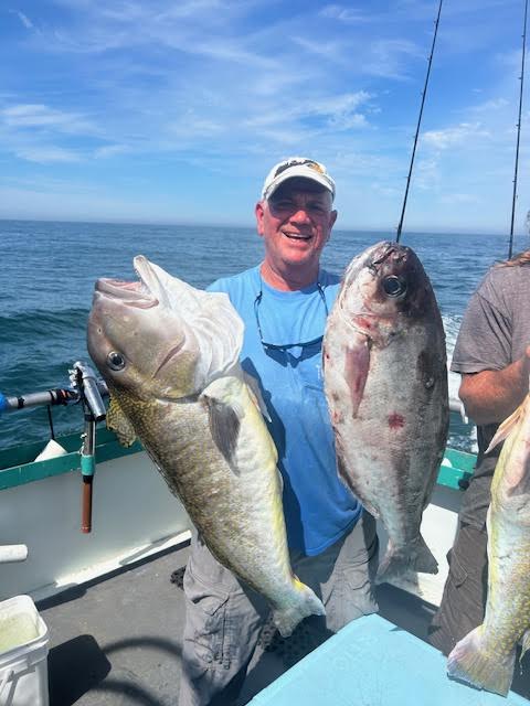 Man on boat holding two large fish with ocean in background.