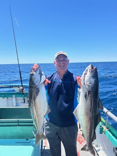 Person on a boat holding two large fish with the ocean in the background.