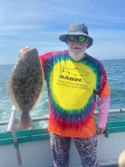 Person in colorful shirt holding a large flatfish on a boat.