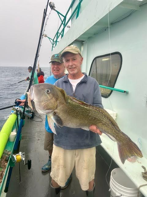 Two men on boat holding a large fish, smiling at camera.