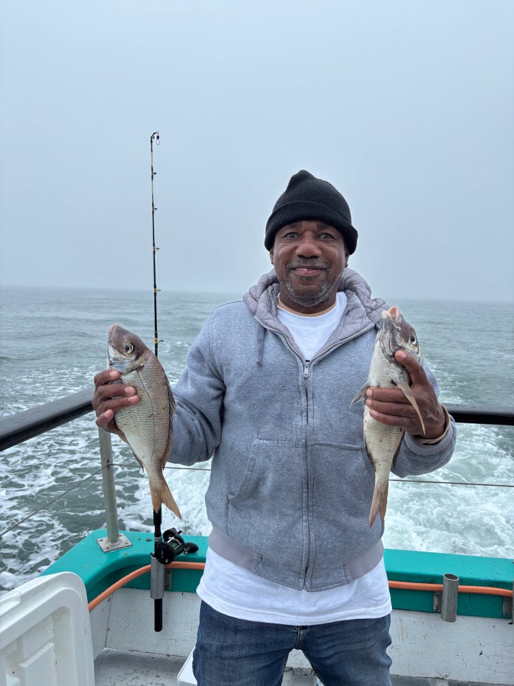 Man holding two fish on a boat in overcast weather.