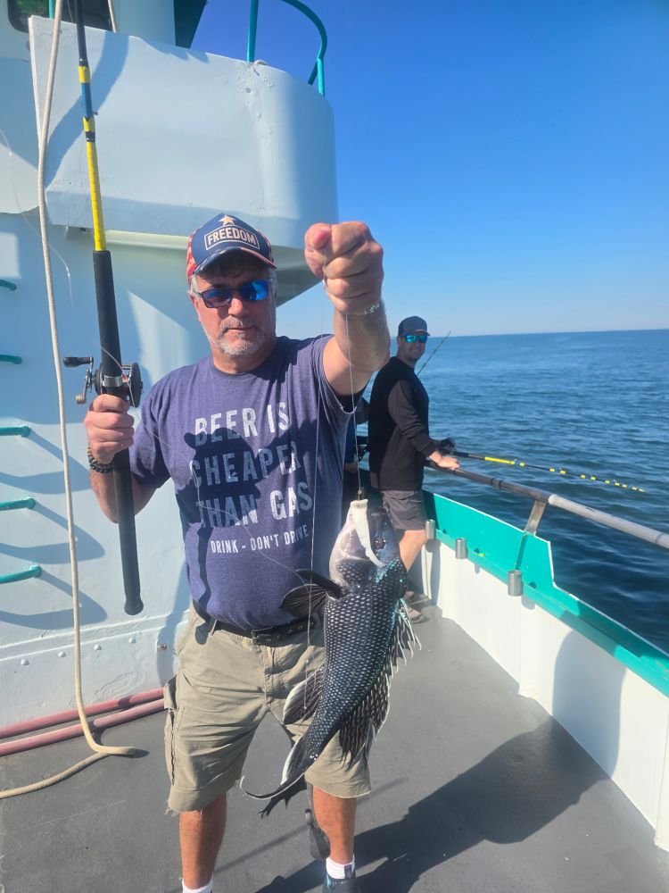 Man on a boat holding a fishing rod and a caught fish.