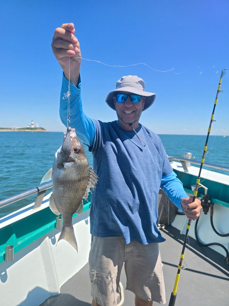 Man on boat holding a fish with a fishing rod, ocean in background.