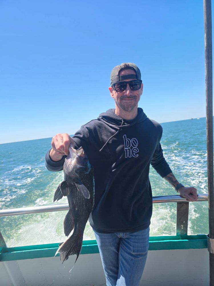 Man holding a fish on a boat under a clear blue sky.