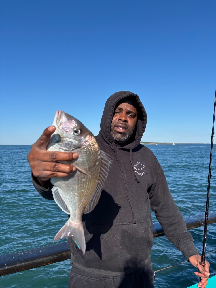Man holding a fish by the ocean with a fishing rod.