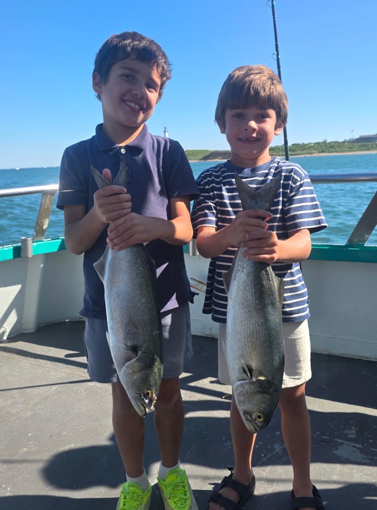 Two smiling boys on a boat holding large fish under a clear sky.