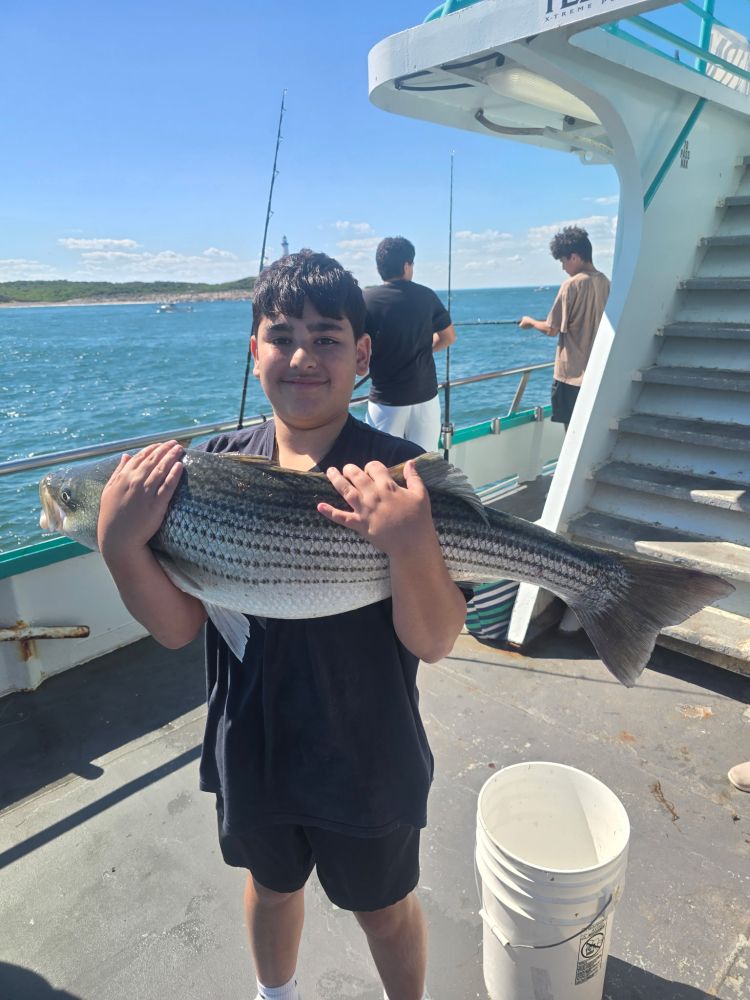 Boy holding a large striped fish on a boat with ocean in background.