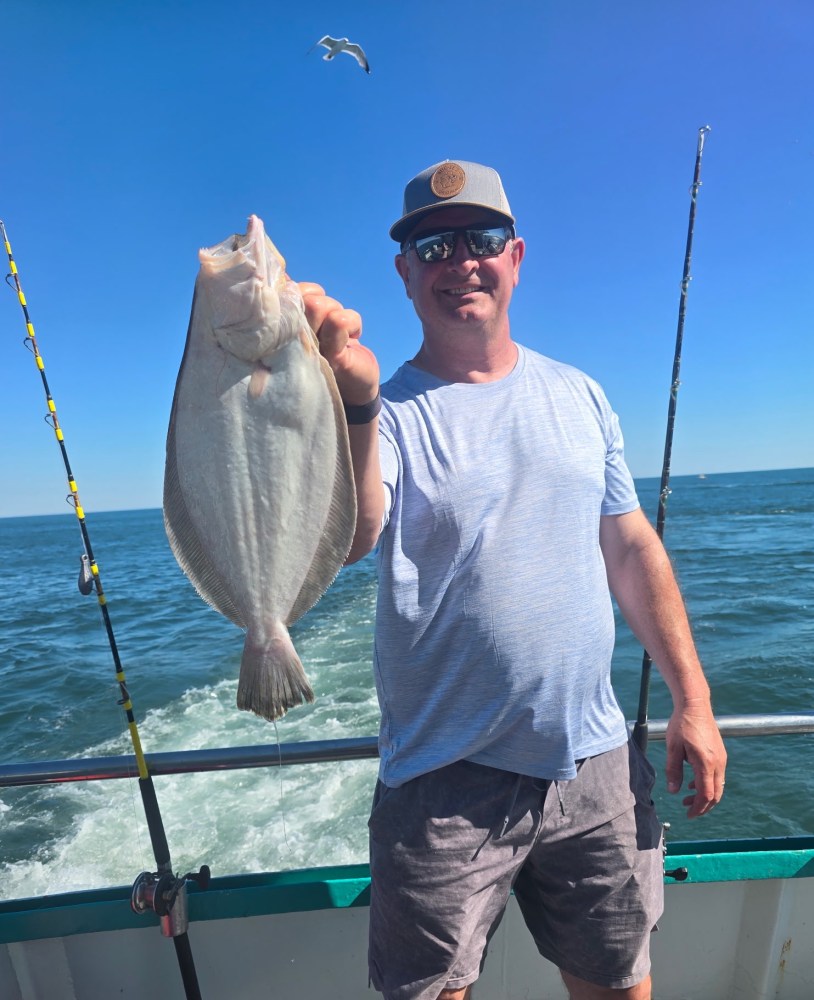 Man on a boat holding a fish with the ocean in the background.