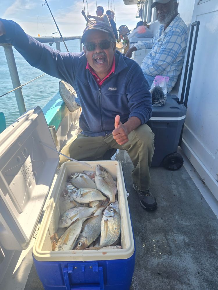 Man on boat smiling, thumbs up, with cooler full of fish.
