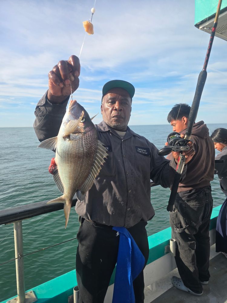 Man holding a fish on a boat with ocean background.