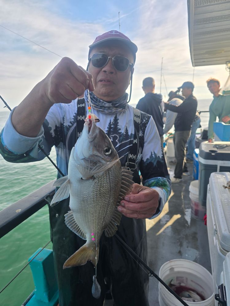 Person holding a large fish on a boat, wearing sunglasses and a cap.