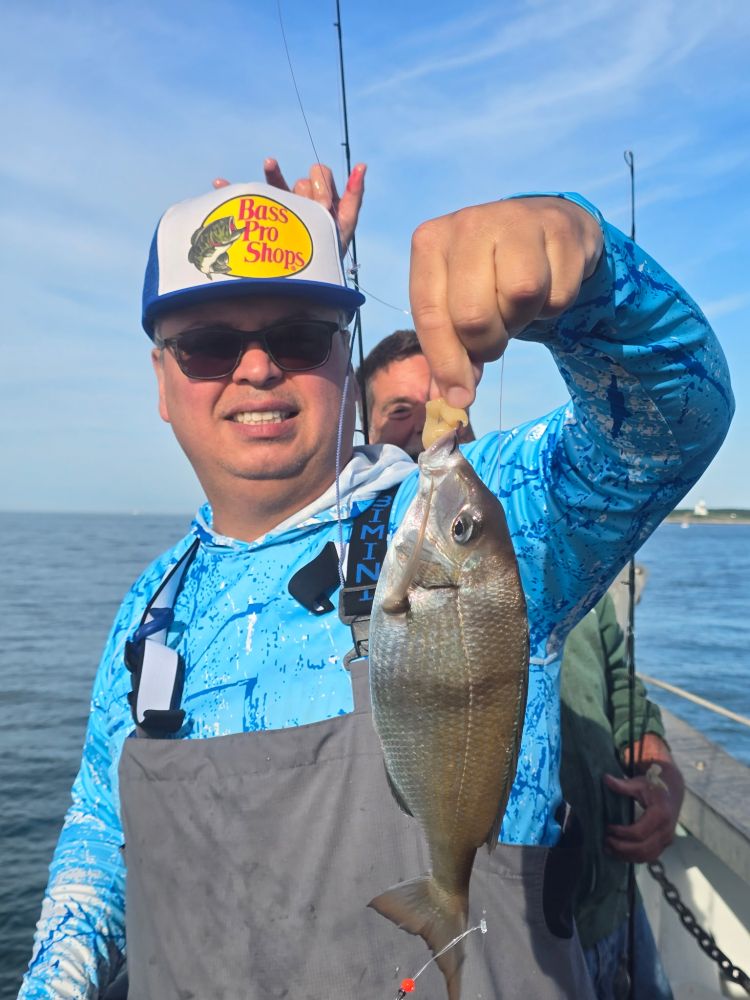 Man on boat holding fish, wearing blue shirt and cap.