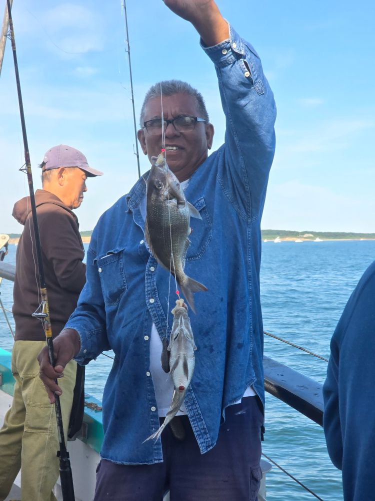 Person holding two fish on a fishing line on a boat.