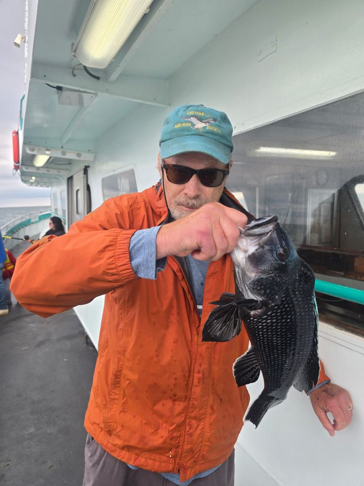 Man holding a fish on a boat, wearing an orange jacket and green cap.