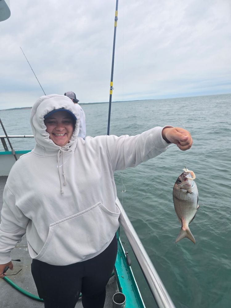 Person in white hoodie holding a fish on a boat with water in the background.