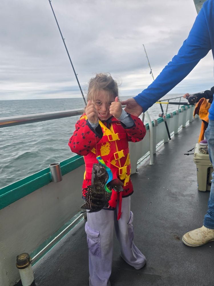 Child on boat holding a fish, smiling with thumbs up.