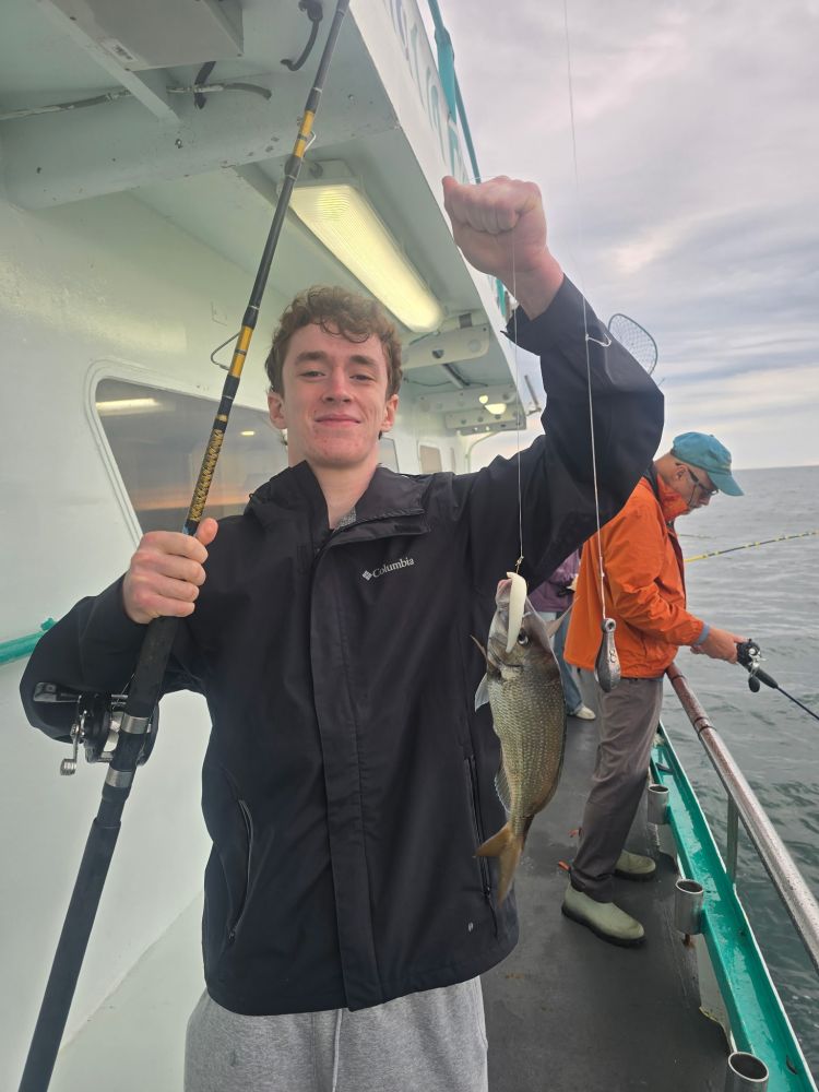 Person holding a fishing rod with a caught fish on a boat.