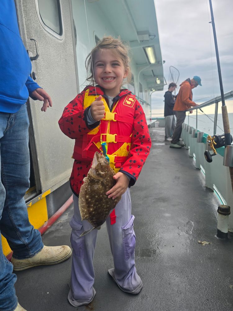 Young child on a boat holding a fish, wearing a red life jacket.