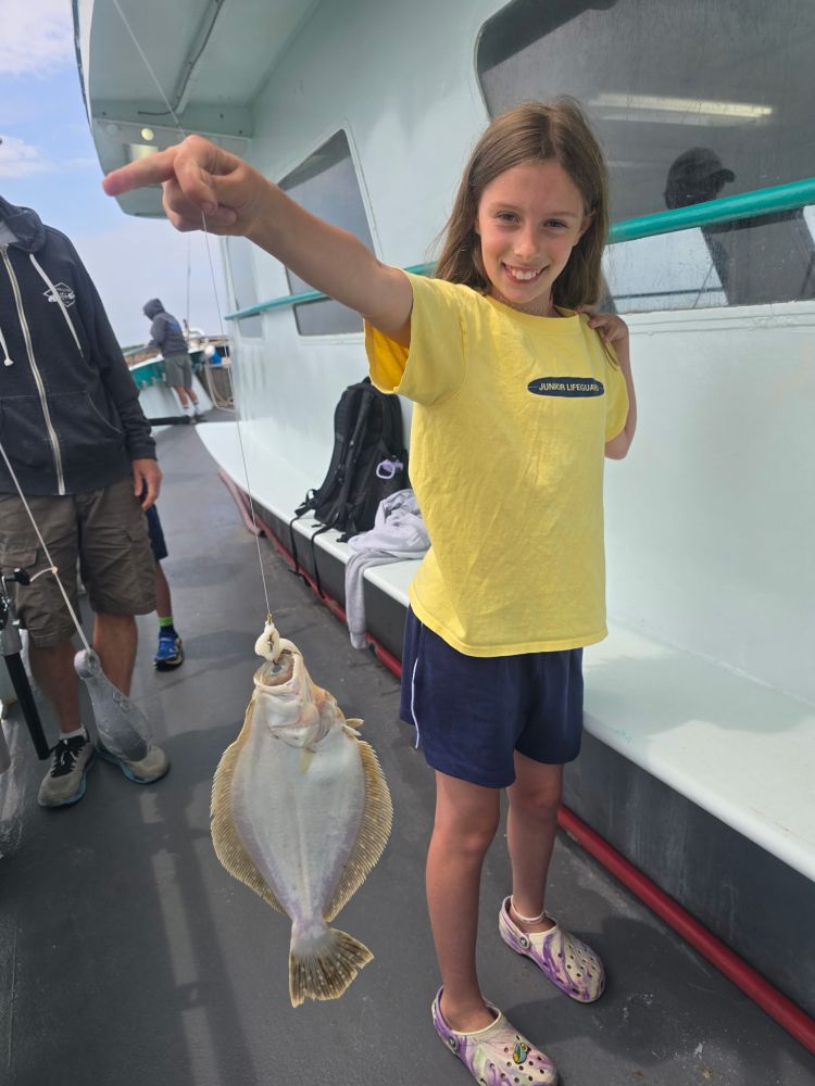 Girl on boat holding up a fish she caught, smiling.
