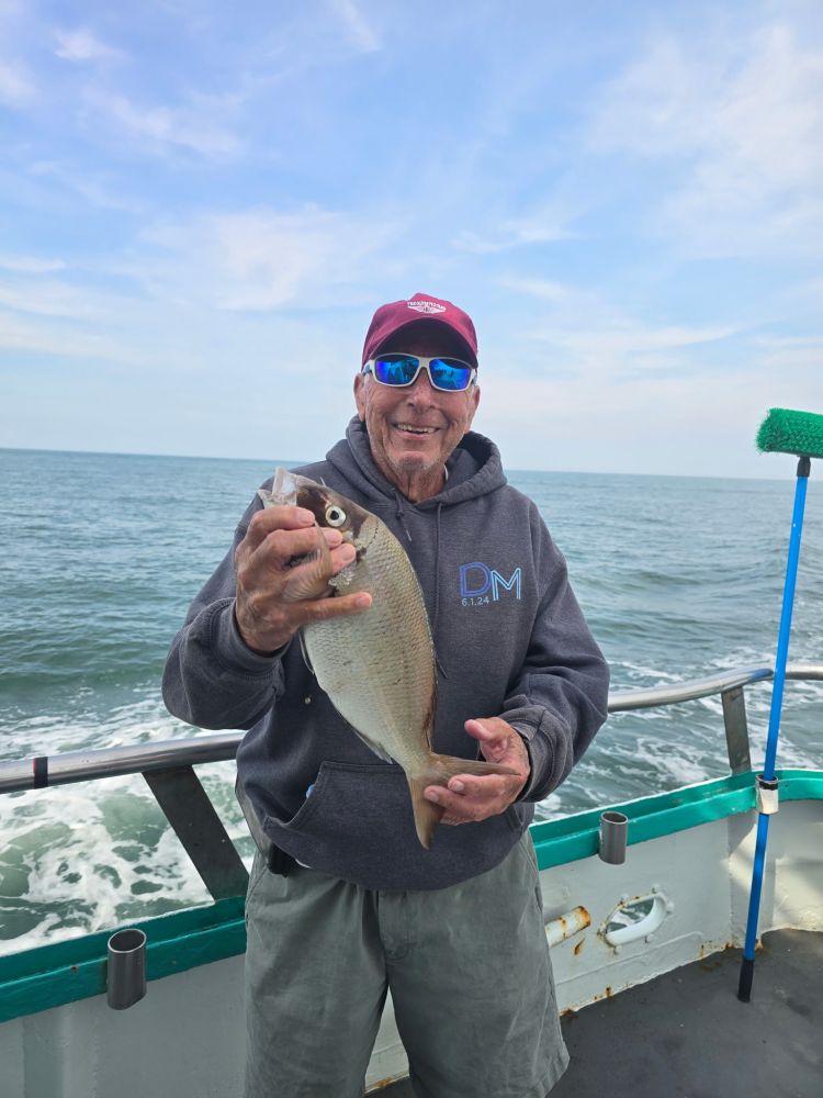 Man on boat holding a fish, smiling, wearing sunglasses and a cap.