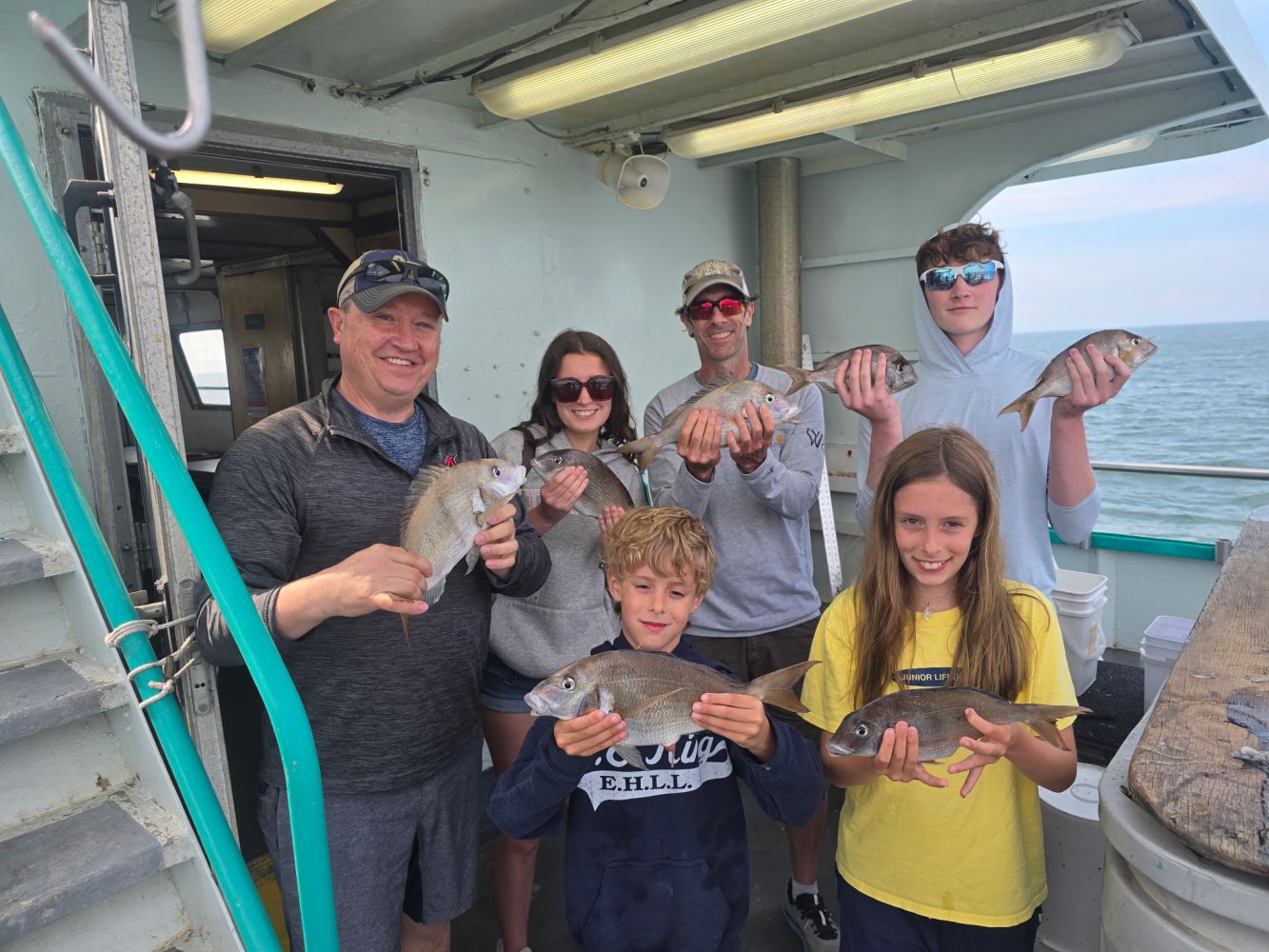 Group on a boat holding fish, smiling at the camera.
