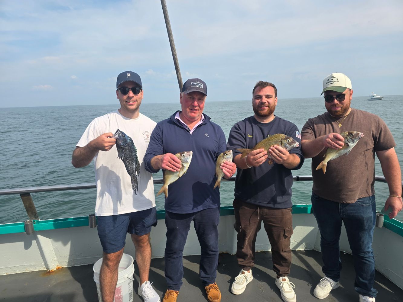 Four men on a boat holding fish, smiling at the camera.