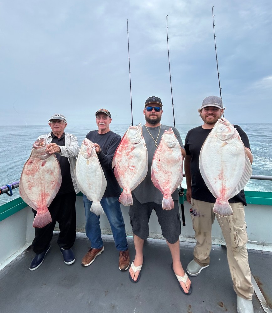 Four men on a boat holding large fish against a cloudy sky.
