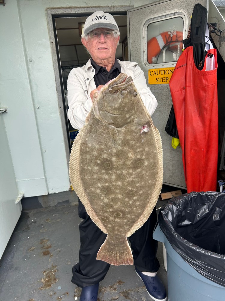 Elderly person holding a large flatfish on a boat.