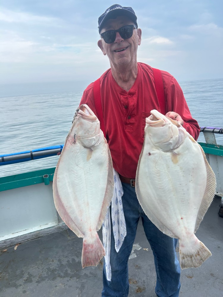 Man on boat holding two large flat fish, smiling.