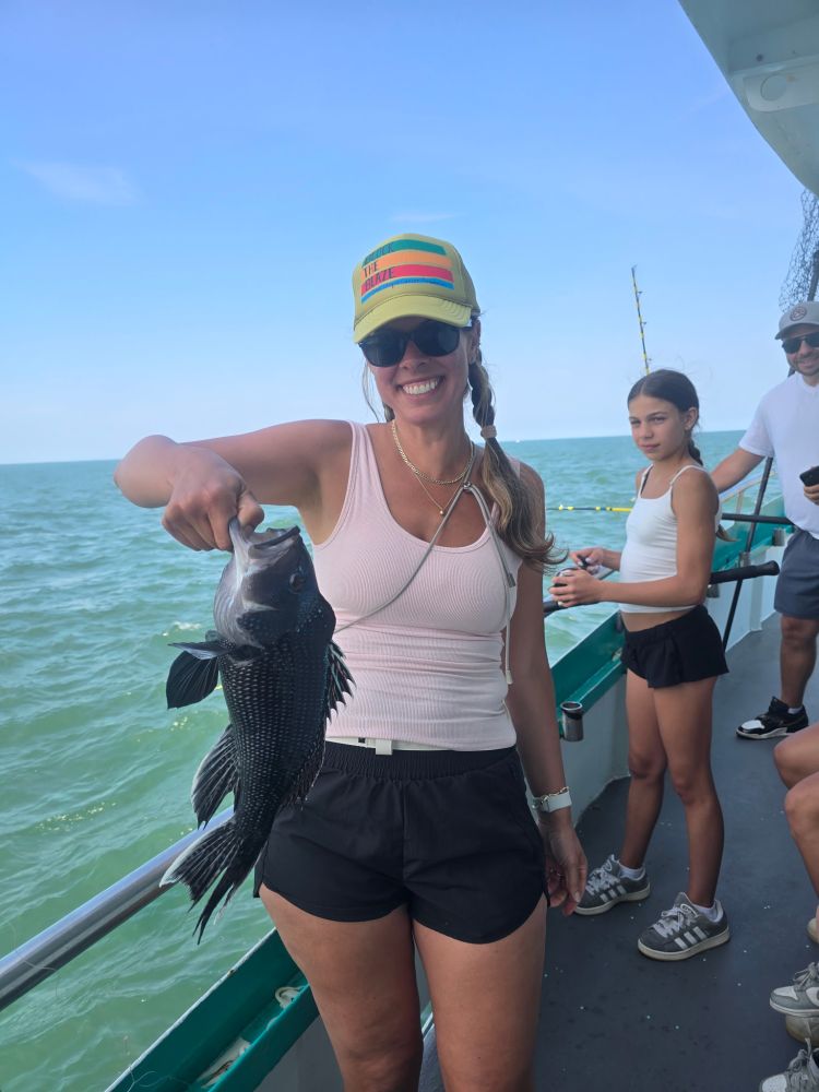 Woman holding a fish on a boat with ocean in the background.