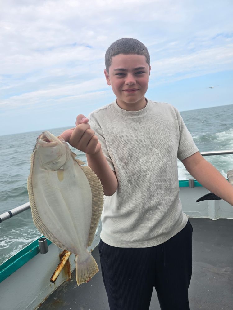 Person holding a flat fish on a boat with the ocean in the background.