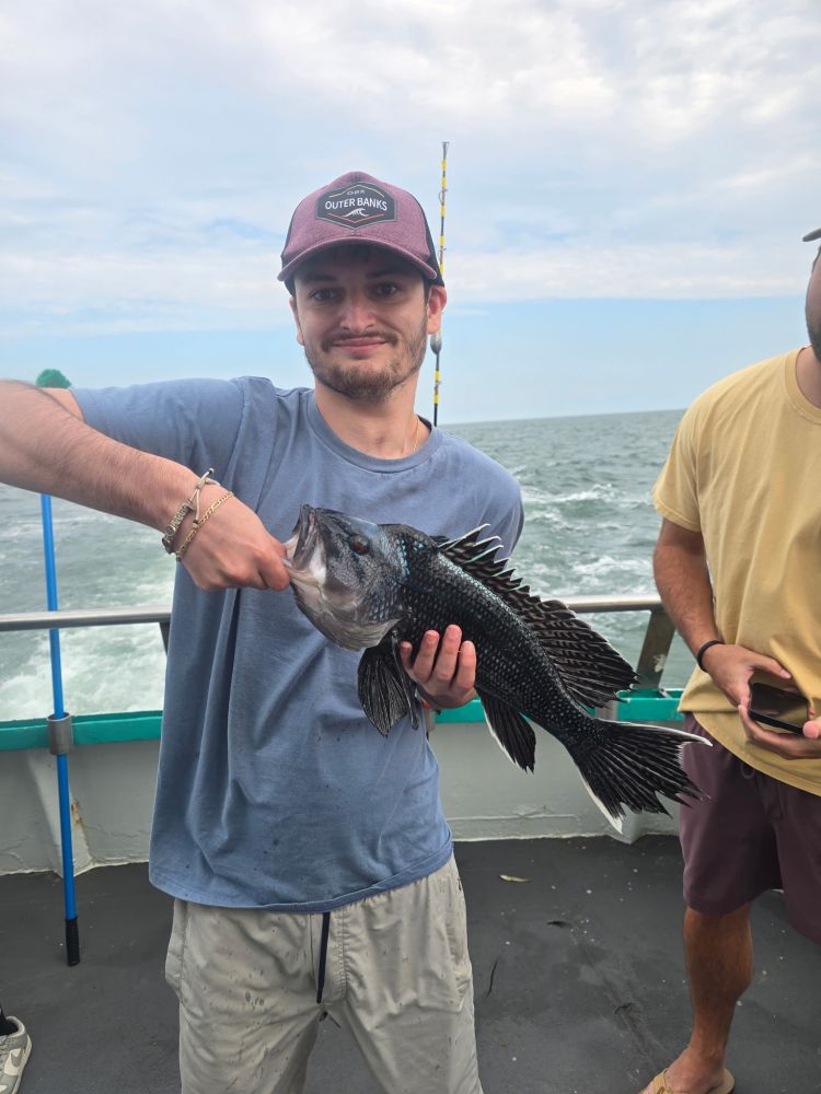 Man holding a black fish on a boat with ocean background.