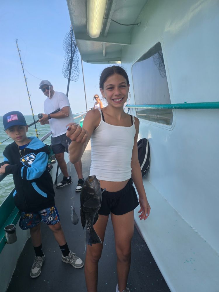 Girl on boat holding a fish, with a boy and man in the background.