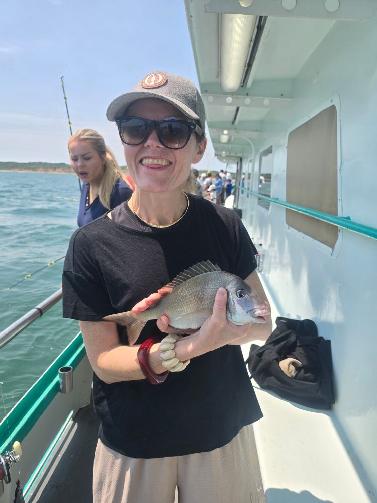 Woman smiling with a fish on a boat with another person in background.
