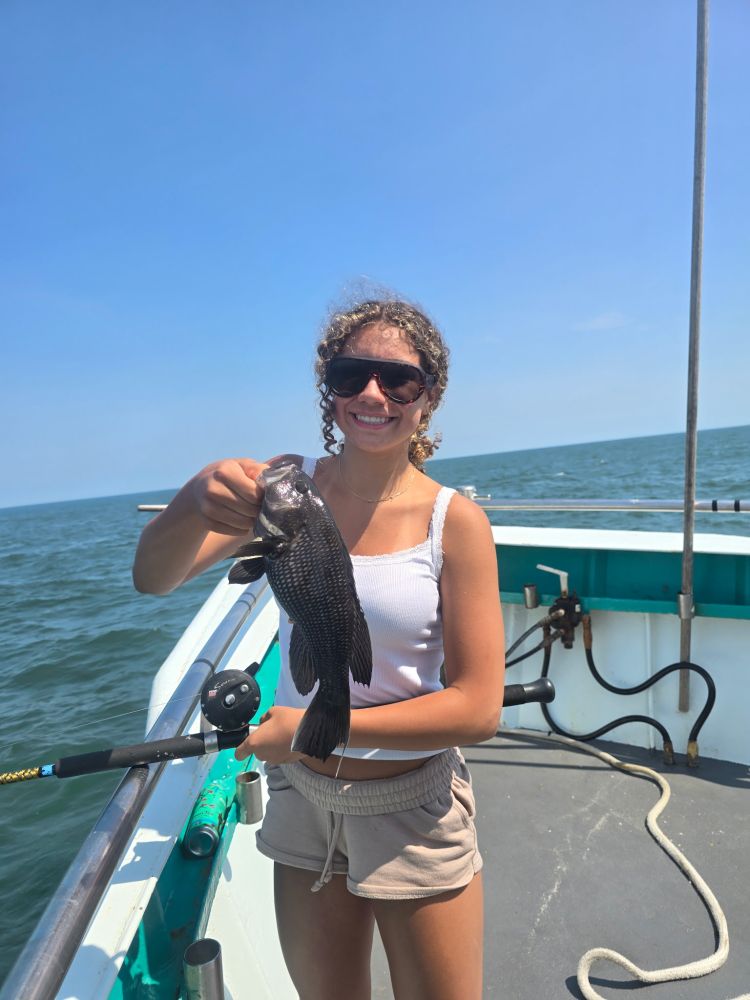 Person smiling, holding a fish on a boat under a clear sky.