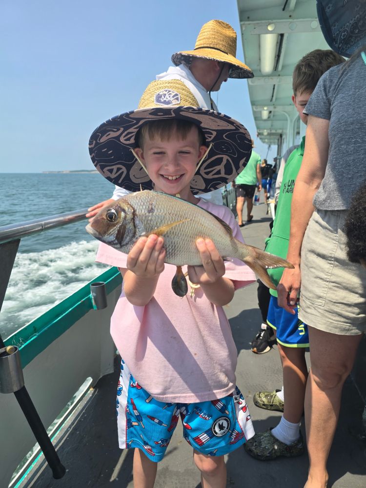 Smiling boy in hat holding fish on boat with others nearby.