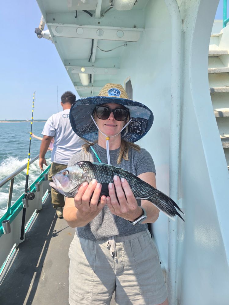 Person holding a fish on a boat, wearing a sun hat and sunglasses.